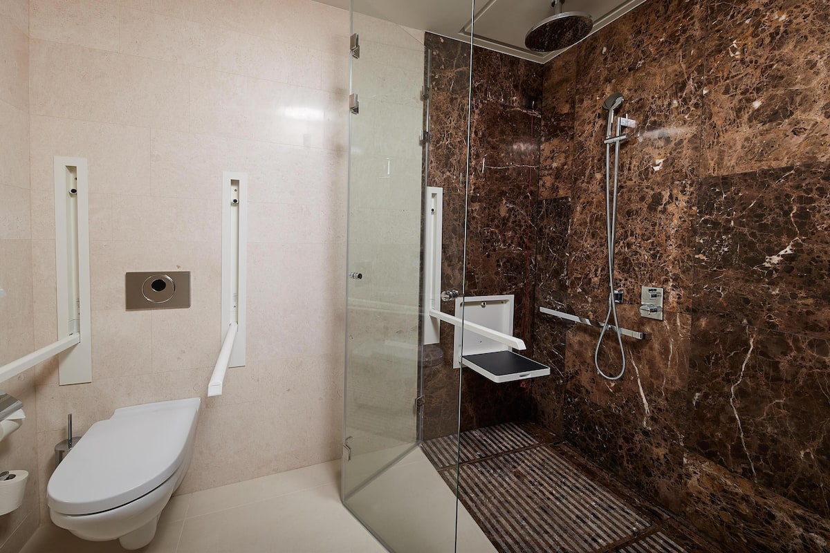 Un baño con inodoro, ducha con cerramiento de vidrio y paredes de mármol.