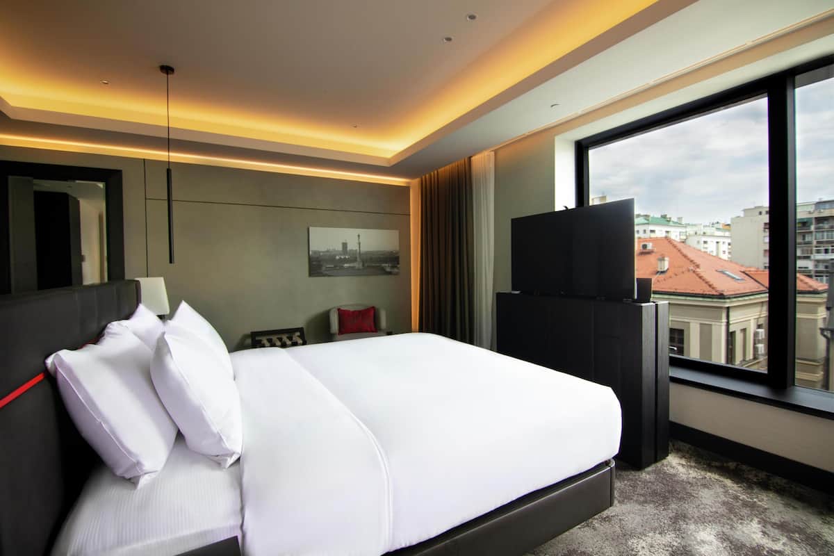 Habitación de hotel con una cama grande, televisión, vista a la ciudad y diseño moderno.