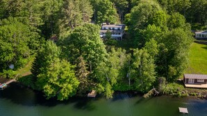 An aerial view of a lakeside property with a large house surrounded by dense forest, a dock, and a small building. - On Silver Lake Close To Woodstock (Barnard)