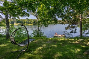 Een hangstoel aan een meer, met een steiger en een stoel aan de overkant.