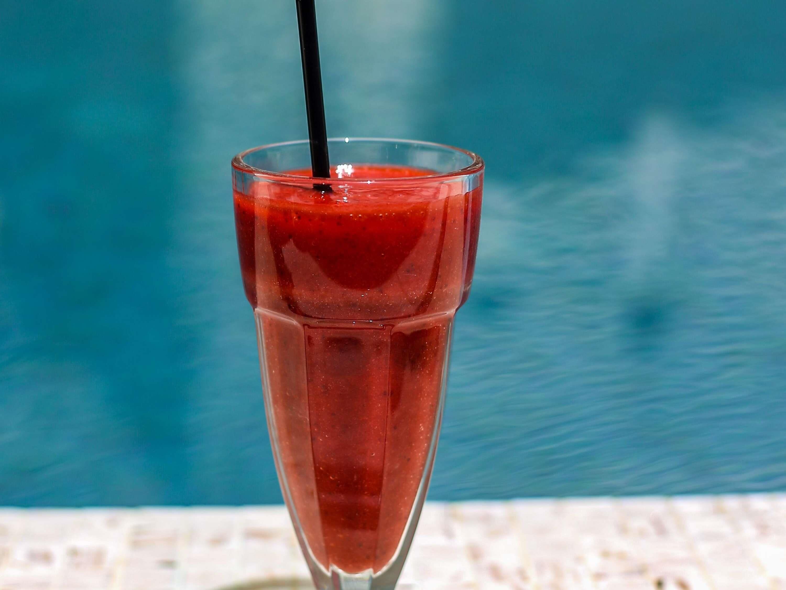 A glass of red drink with a straw by a pool.