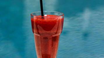 A glass of red drink with a straw by a pool.