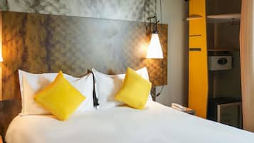 A hotel room with a large bed, two pillows, a headboard with a textured design, a wall-mounted lamp, and a telephone.