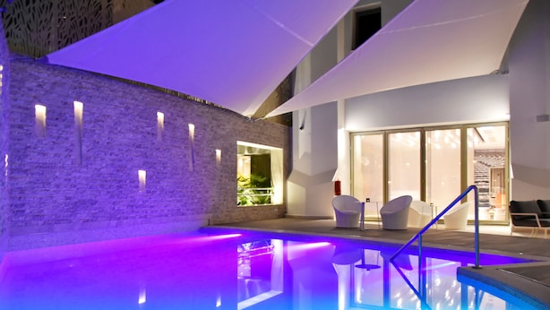 A modern indoor pool area with a brick wall, seating by the pool, and a glass door entrance. - ibis Sfax (Sfax Ouest)