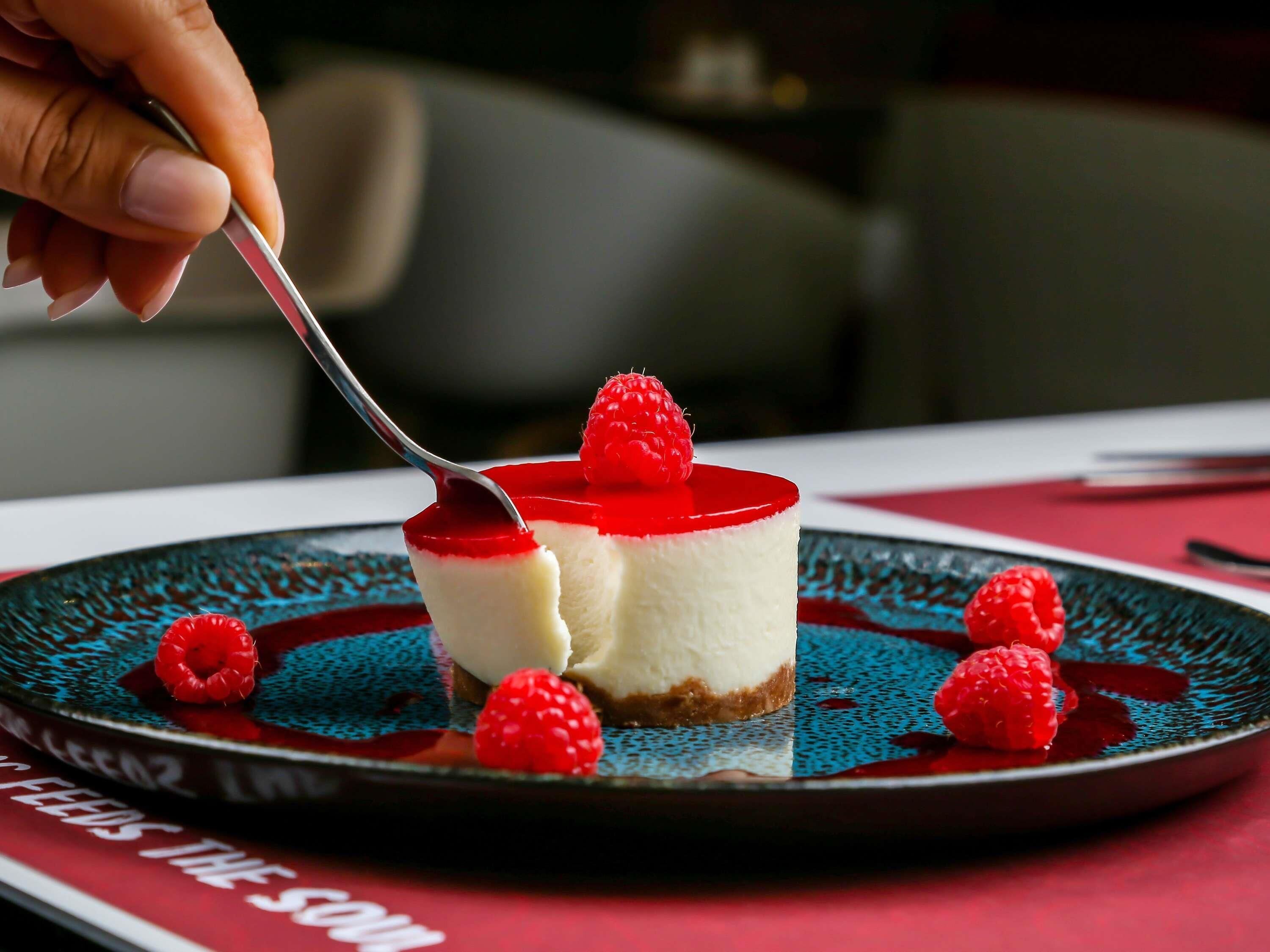 Una porción de pastel de queso con cobertura roja y frambuesas sobre un plato.