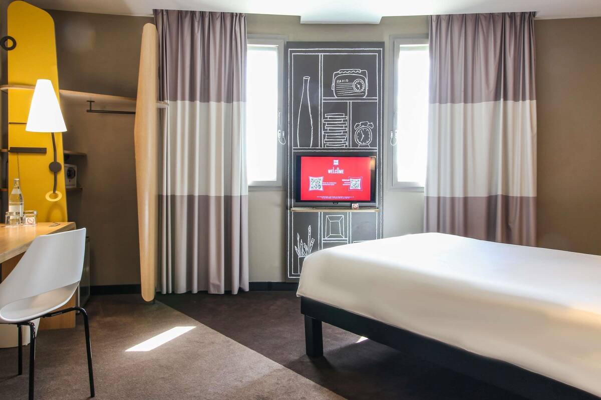 A hotel room with a bed, a desk with a chair, a television, and curtains.