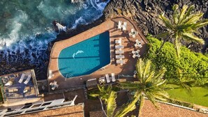 An aerial view of a resort with a swimming pool surrounded by lounge chairs and palm trees, overlooking the ocean. - Poipu Shores 303A - Oceanfront Luxury w/ AC & Pool (Koloa)