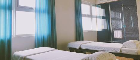 A room with two beds, a shower area, and a window with curtains.