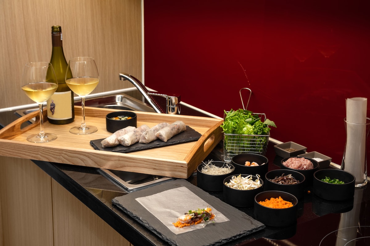 A tray with two glasses of white wine, a bottle of wine, and a wooden board with food items.