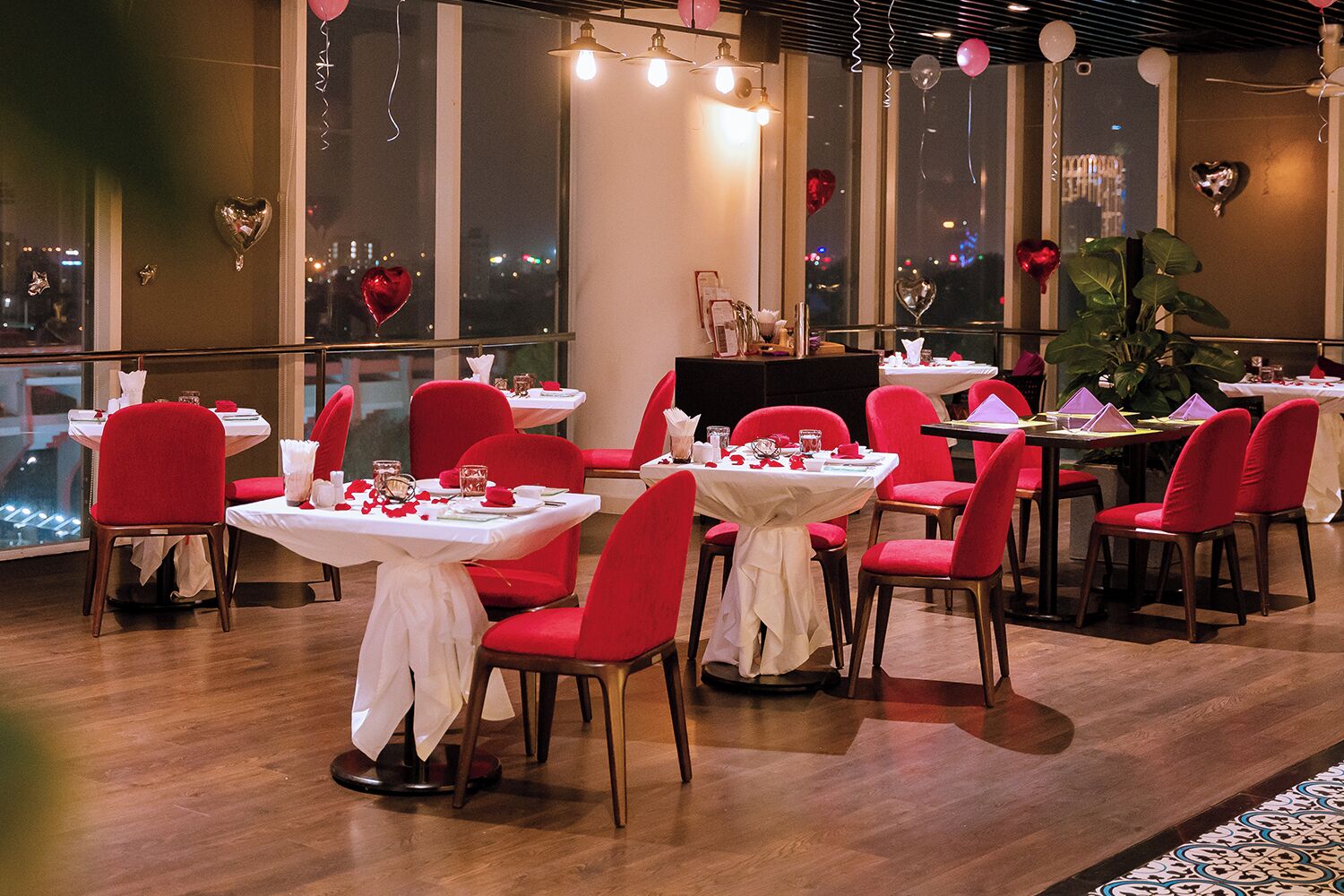 Un restaurant amb cadires vermelles i tovalloles blanques, grans finestres i decoracions amb forma de cor.
