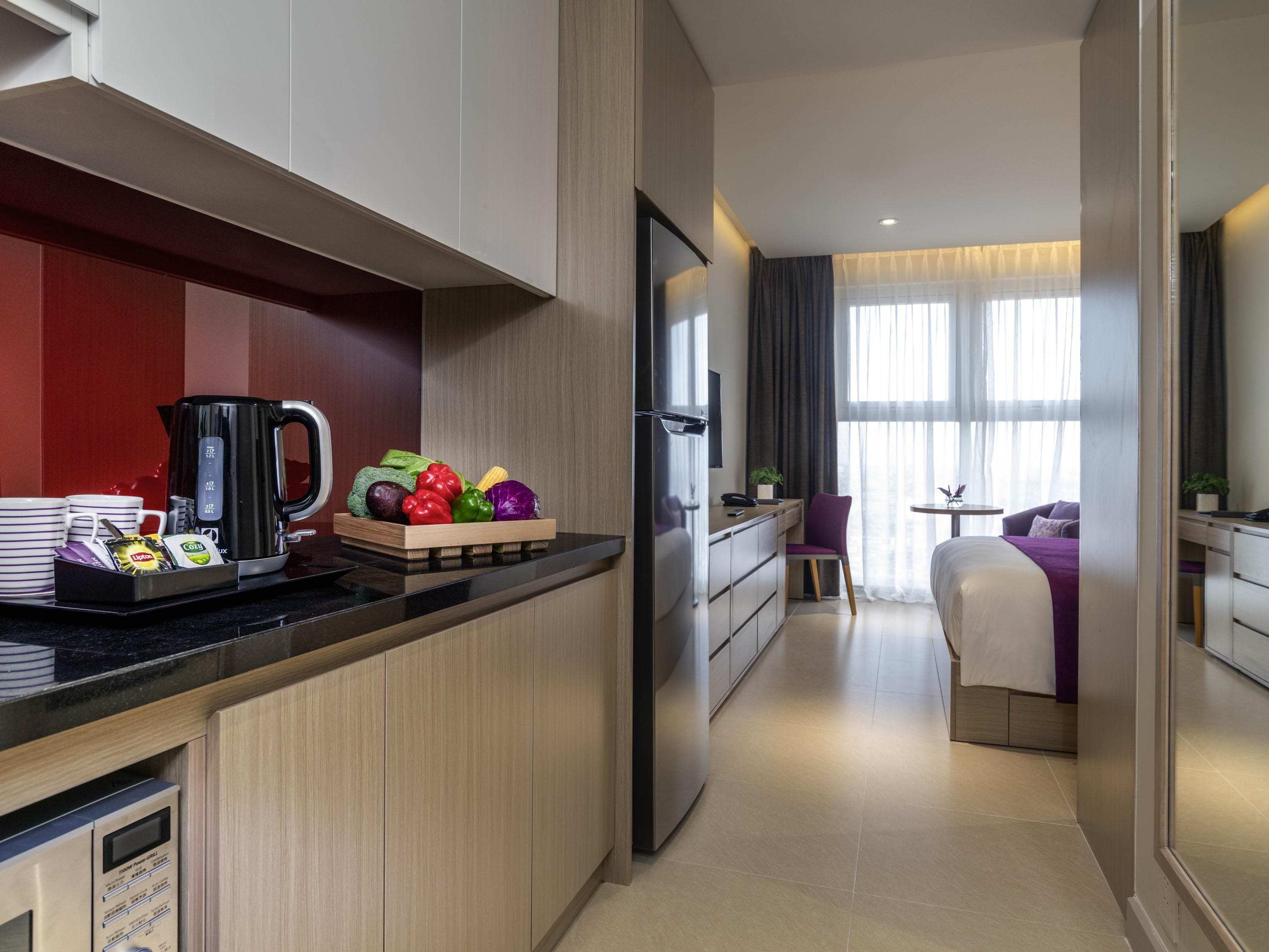 A modern hotel room with a kitchenette, a dining area, and a bed.