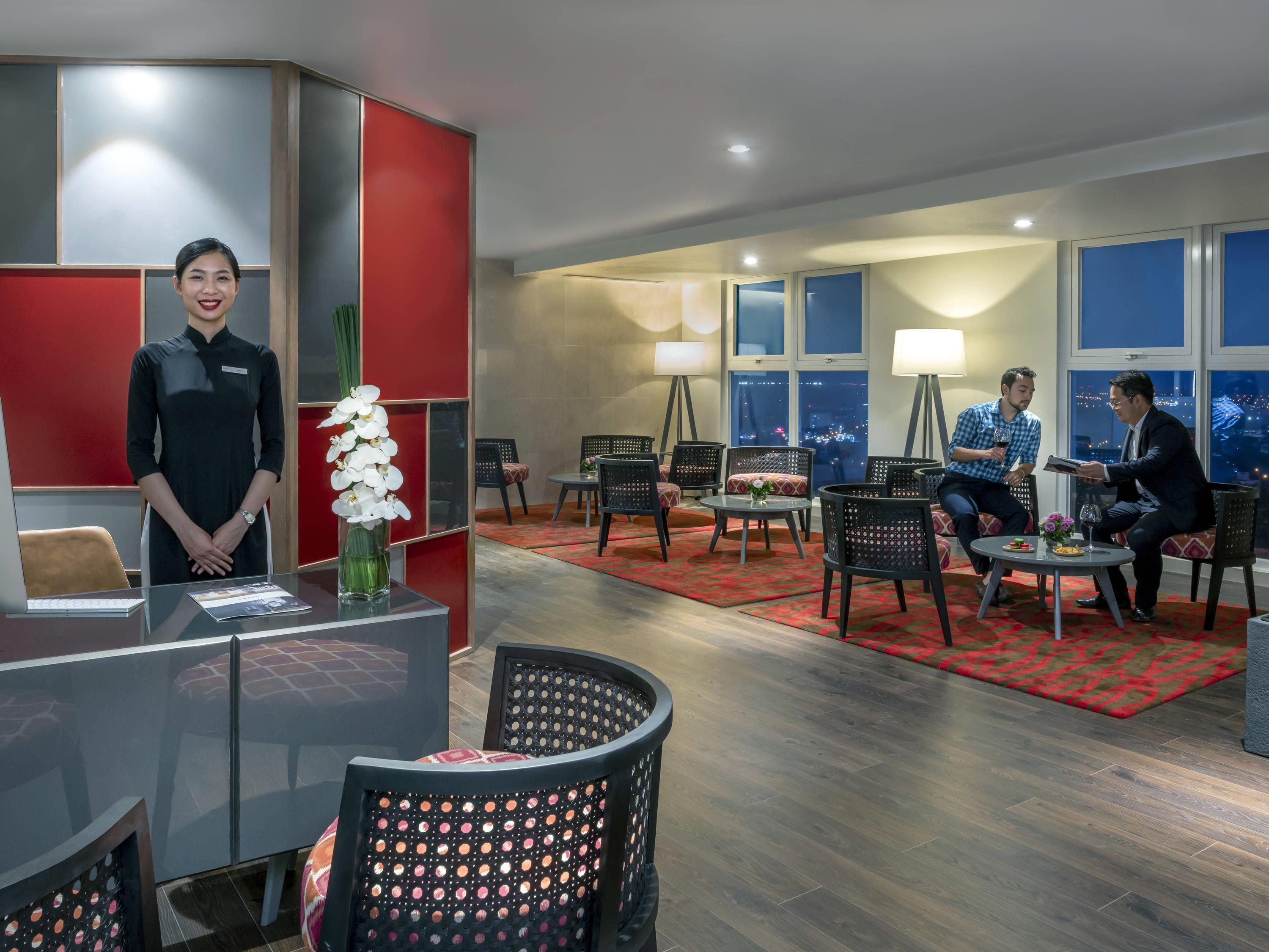 Vestíbulo de hotel con una recepción, zona de estar y grandes ventanales con vistas a la ciudad.