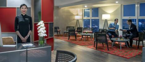 Vestíbulo de hotel con una recepción, zona de estar y grandes ventanales con vistas a la ciudad.