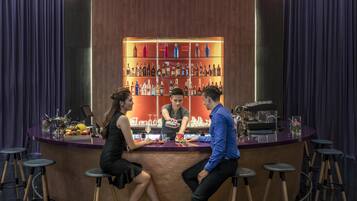 En bardisk med en bartender som blandar drinkar, en sittande kvinna och en man i en blå skjorta.