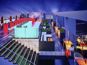 A modern rooftop bar with multiple seating areas, a bar counter, and a view of the cityscape.