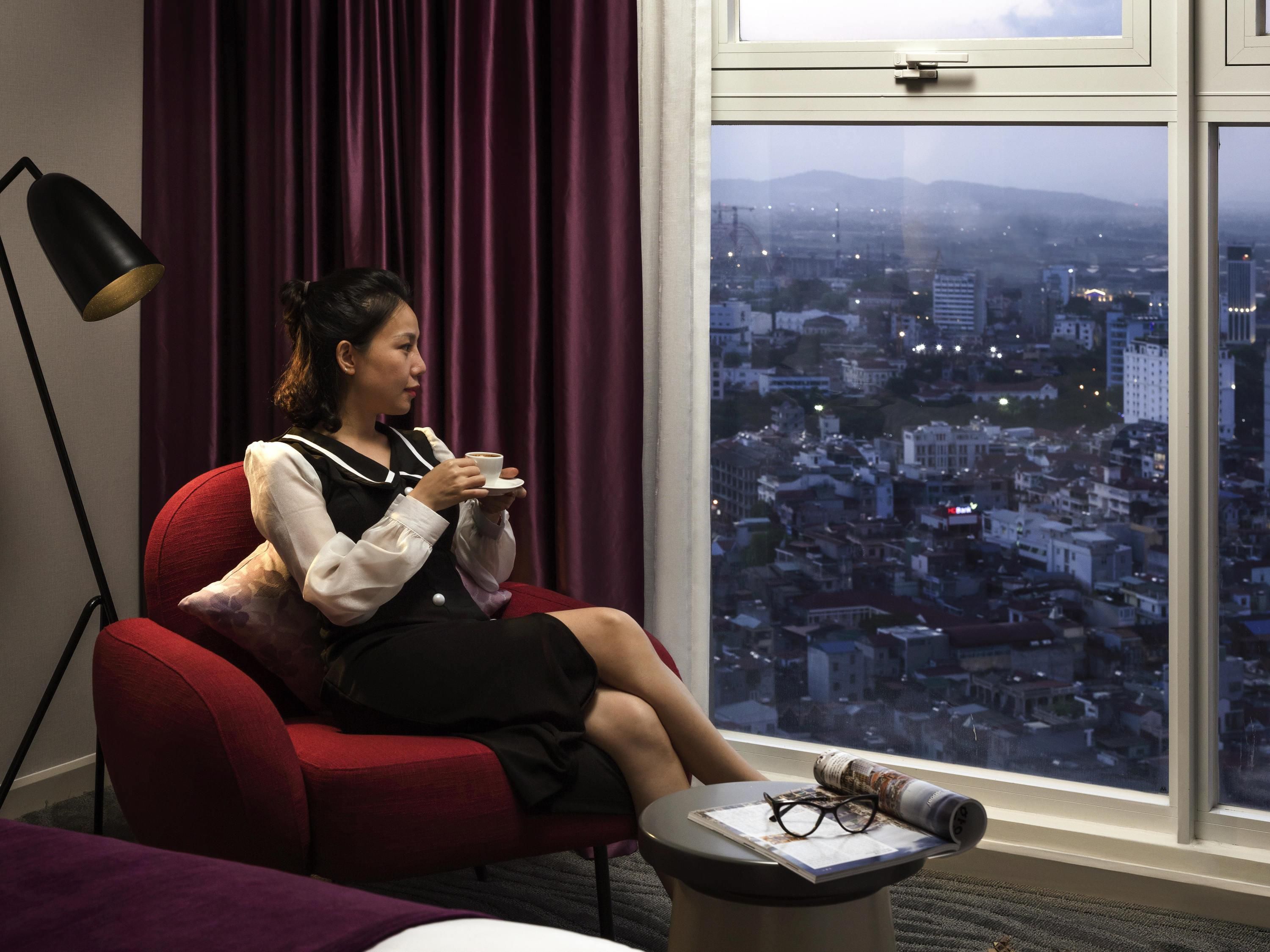 A person seated in a red chair by a window with a cityscape view.