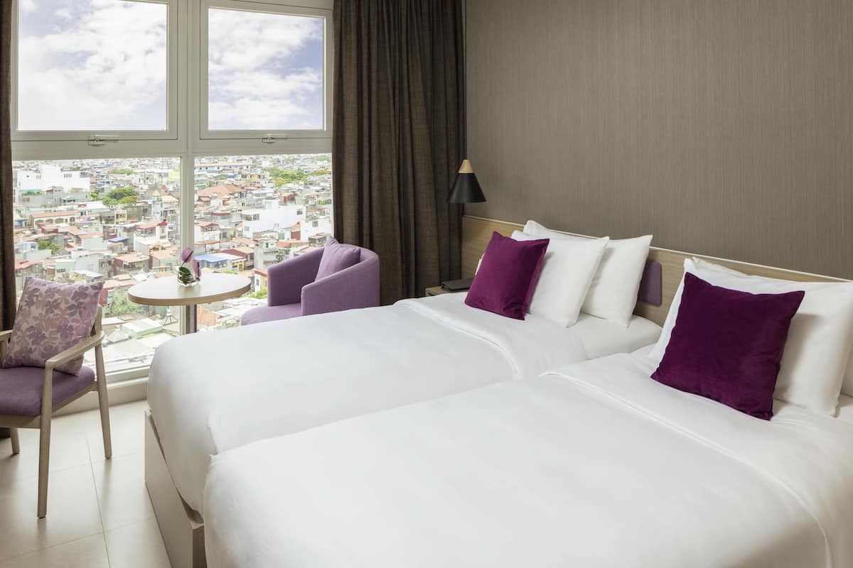 Een hotelkamer met twee bedden, een stoel, een tafeltje en uitzicht op de stad.