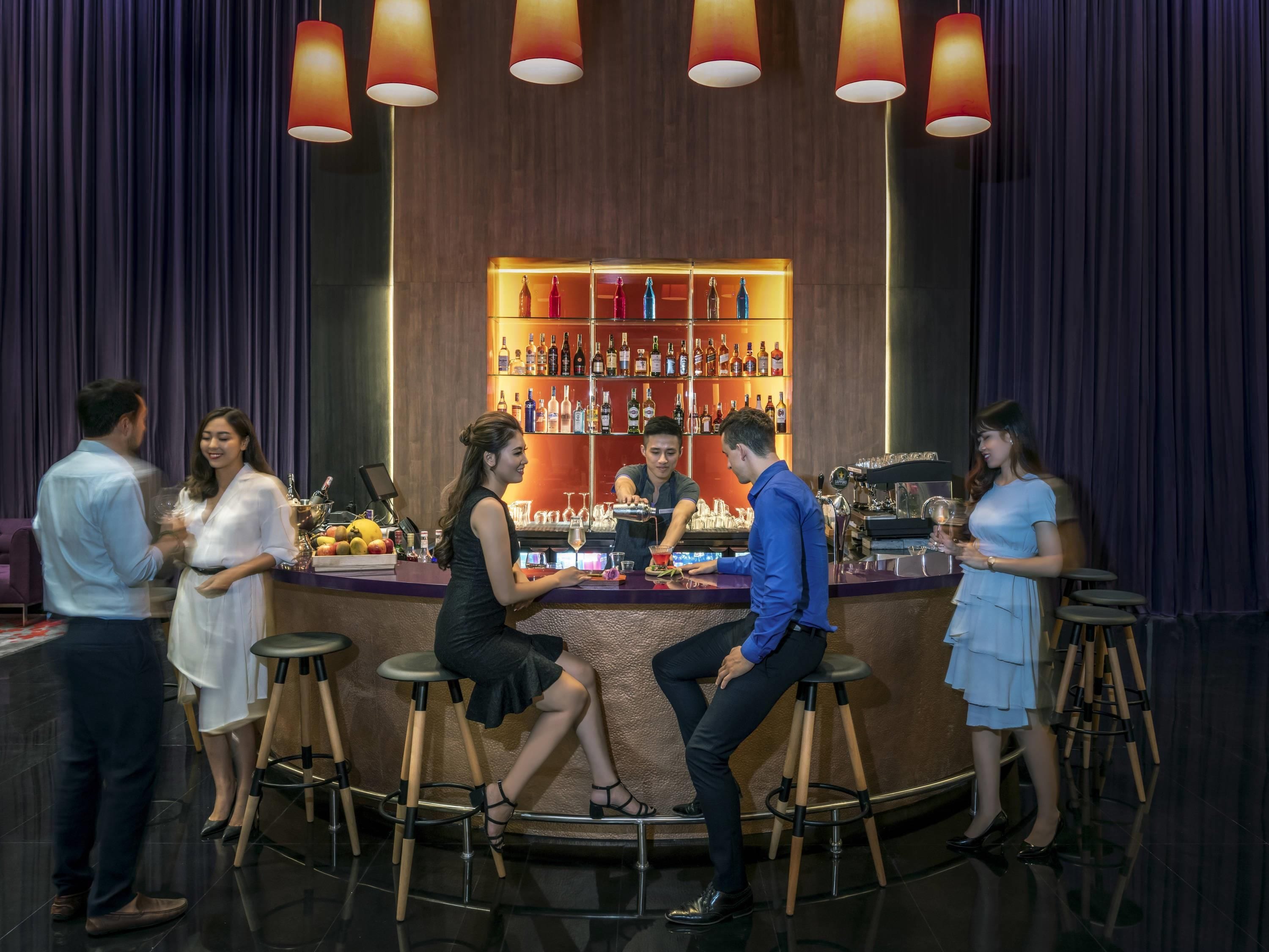 A bar area with stools, a bartender, and a well-stocked shelf of bottles.