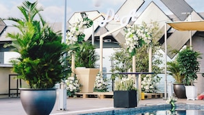Zwembad met potplanten en een zonnescherm, omringd door een modern gebouw met een geometrisch gevelontwerp.