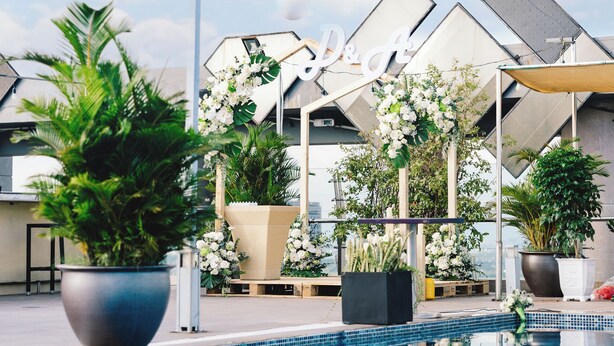 Zwembad met potplanten en een zonnescherm, omringd door een modern gebouw met een geometrisch gevelontwerp.