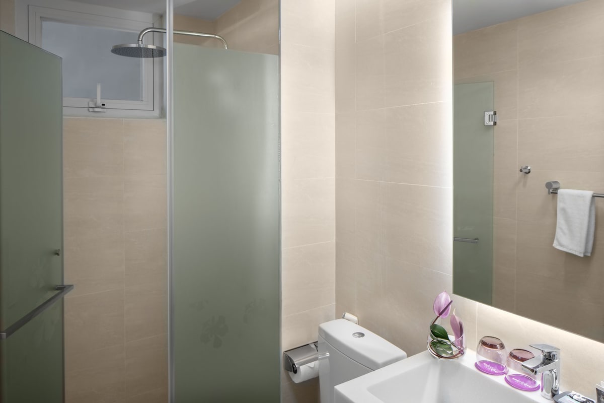 A modern bathroom with a glass shower enclosure, a toilet, and a sink with a mirror.