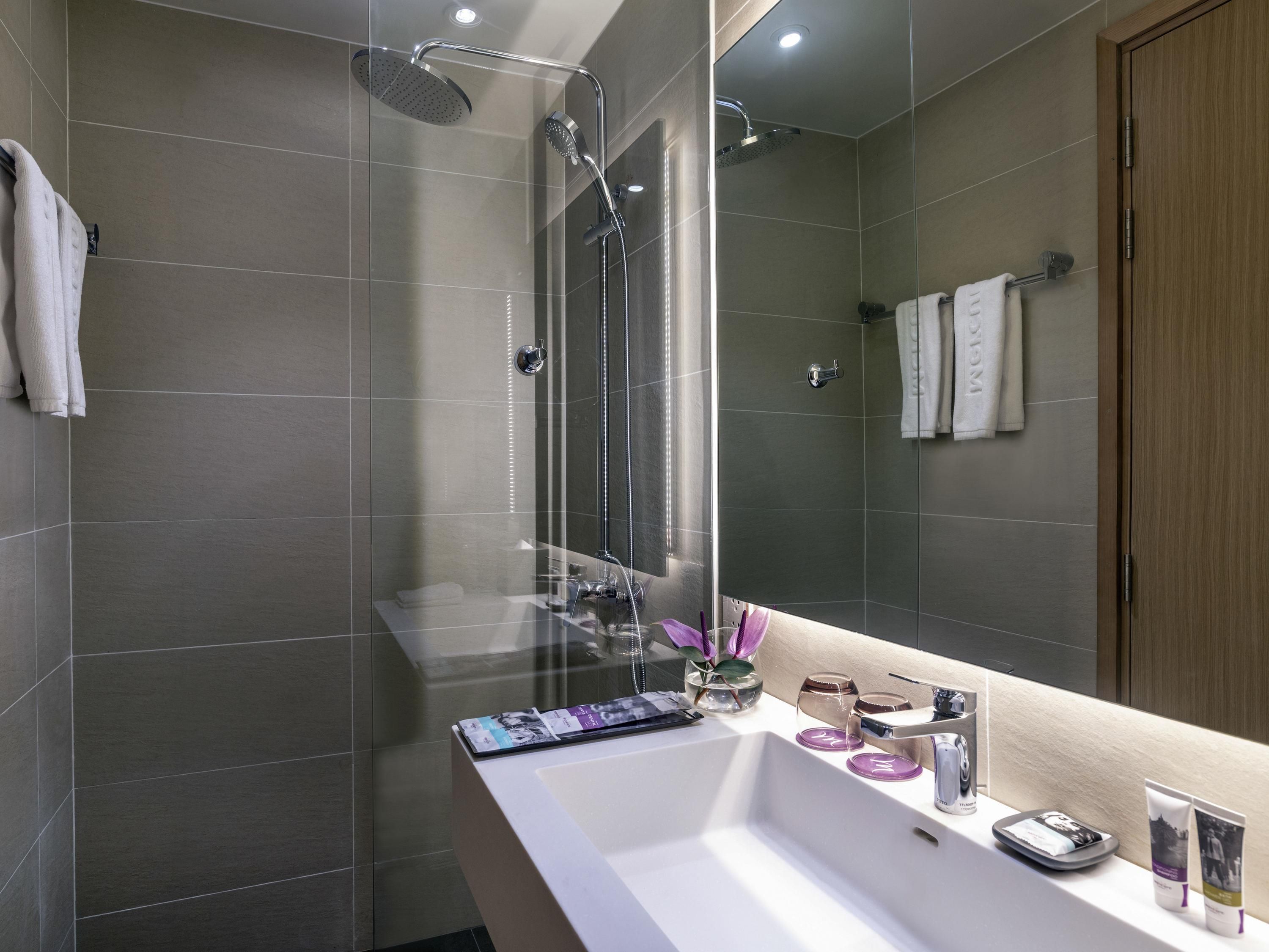 Une salle de bain moderne avec un grand miroir, une douche et un lavabo équipé de produits de toilette.