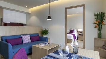Una habitación de hotel moderna con un sofá azul, una mesa de comedor con cubiertos y vasos, un espejo y una planta en maceta.