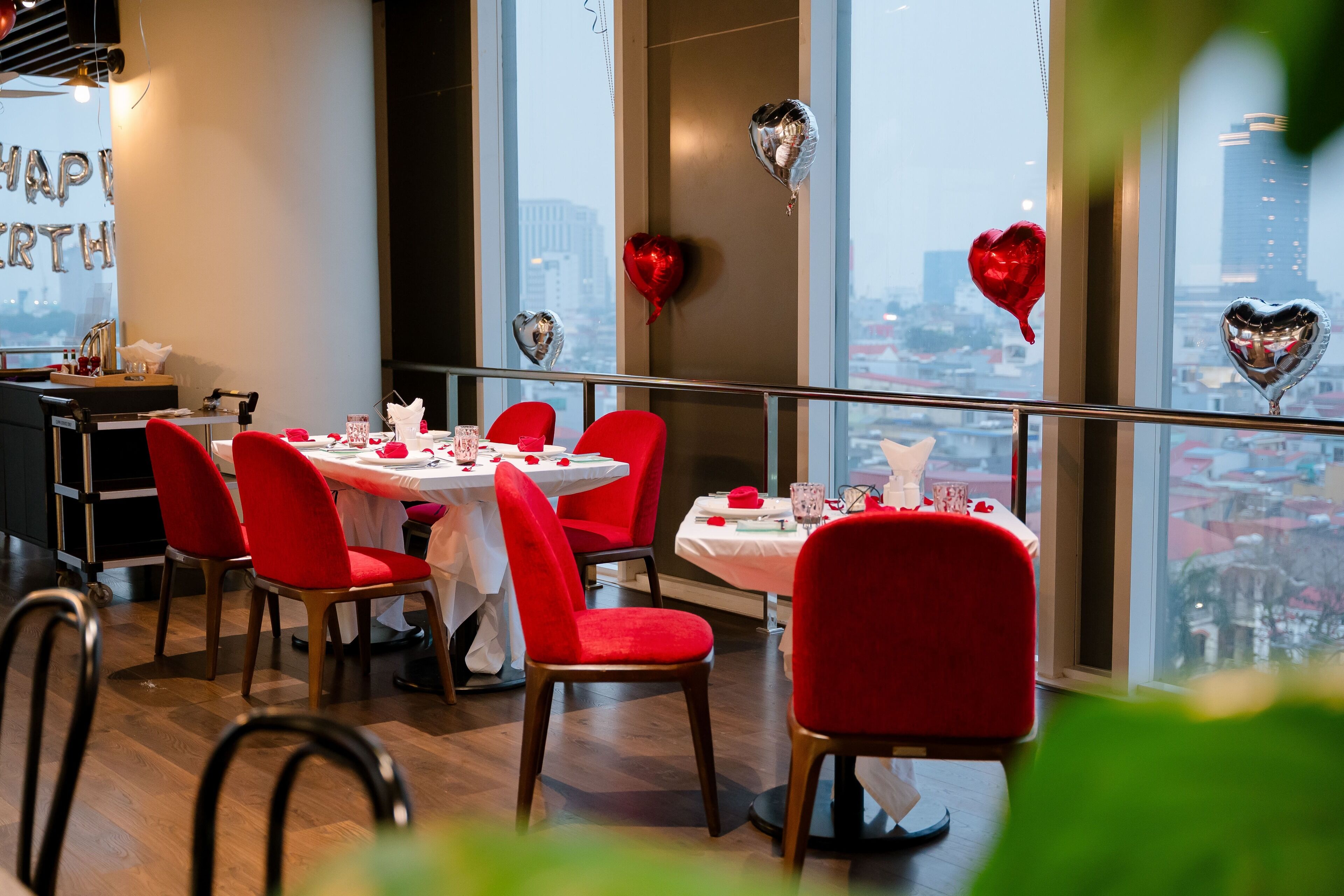 A restaurant with round tables and red chairs, decorated with heart-shaped balloons and a 'Happy Earth Day' sign.