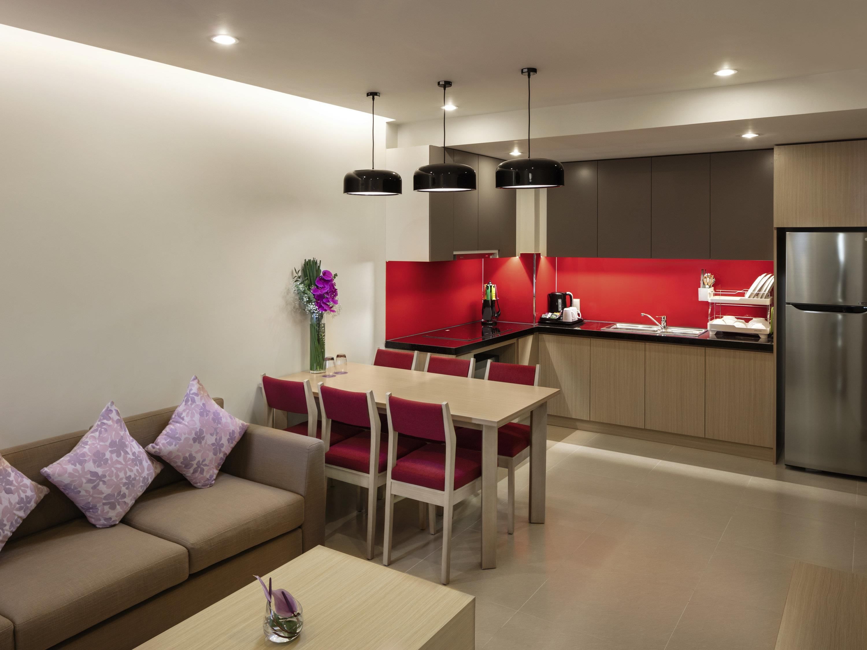 A modern kitchen with a refrigerator, a dining area with a table and chairs, and a sofa with cushions.