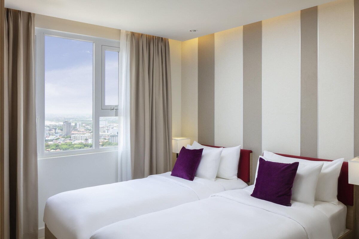 Een hotelkamer met twee bedden, een groot raam en uitzicht op de stad.