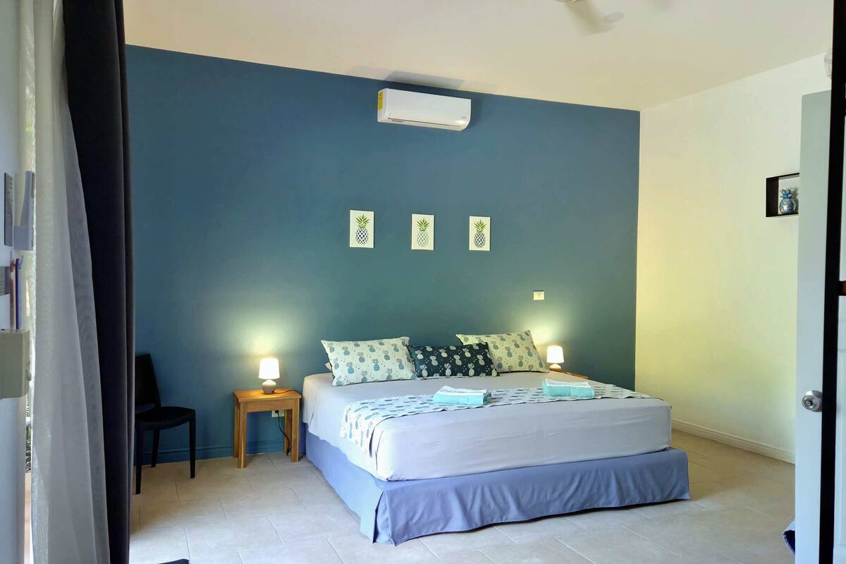 Un dormitorio con una cama, dos mesitas de noche con lámparas, una silla y un aire acondicionado instalado en la pared.