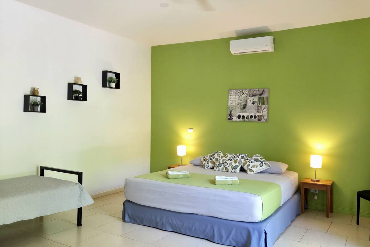 Un dormitorio con cama, lámparas de noche, escritorio, silla y aire acondicionado de pared.