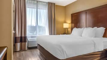 Ein Hotelzimmer mit einem großen Bett, einem Nachttisch, einer Lampe und Blick ins Freie durch ein mit Vorhängen drapiertes Fenster.