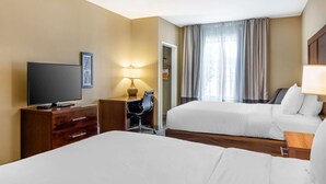 Habitación de hotel con dos camas, un escritorio con televisor, una silla, una lámpara y un armario.