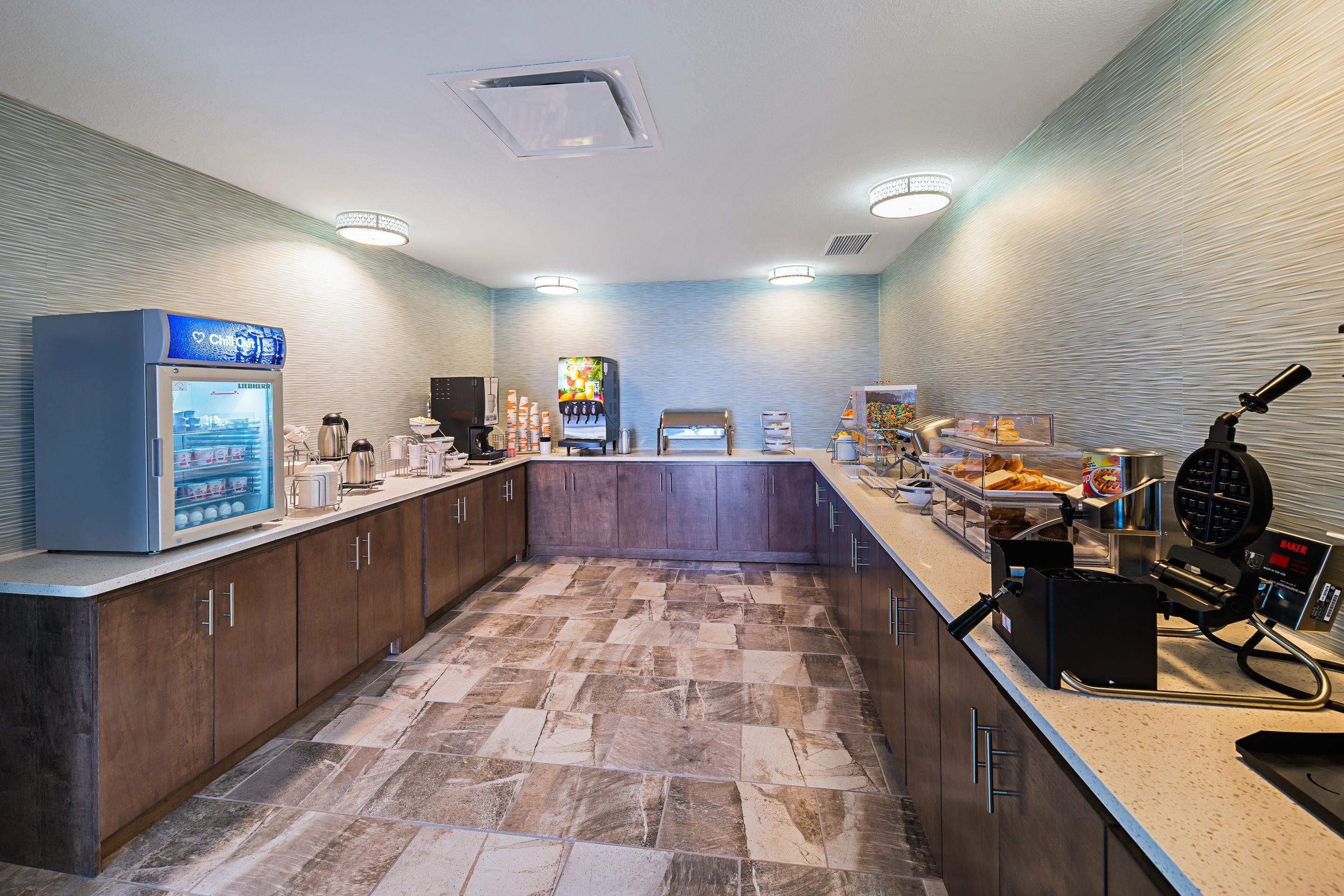 A modern kitchen with a stone tile floor, a coffee machine, a waffle maker, and a refrigerator.