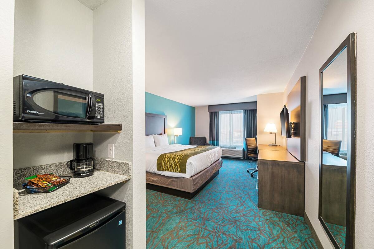 Ein Hotelzimmer mit einem Bett, einem Schreibtisch mit Computer, einer Mikrowelle und einer Kaffeemaschine.