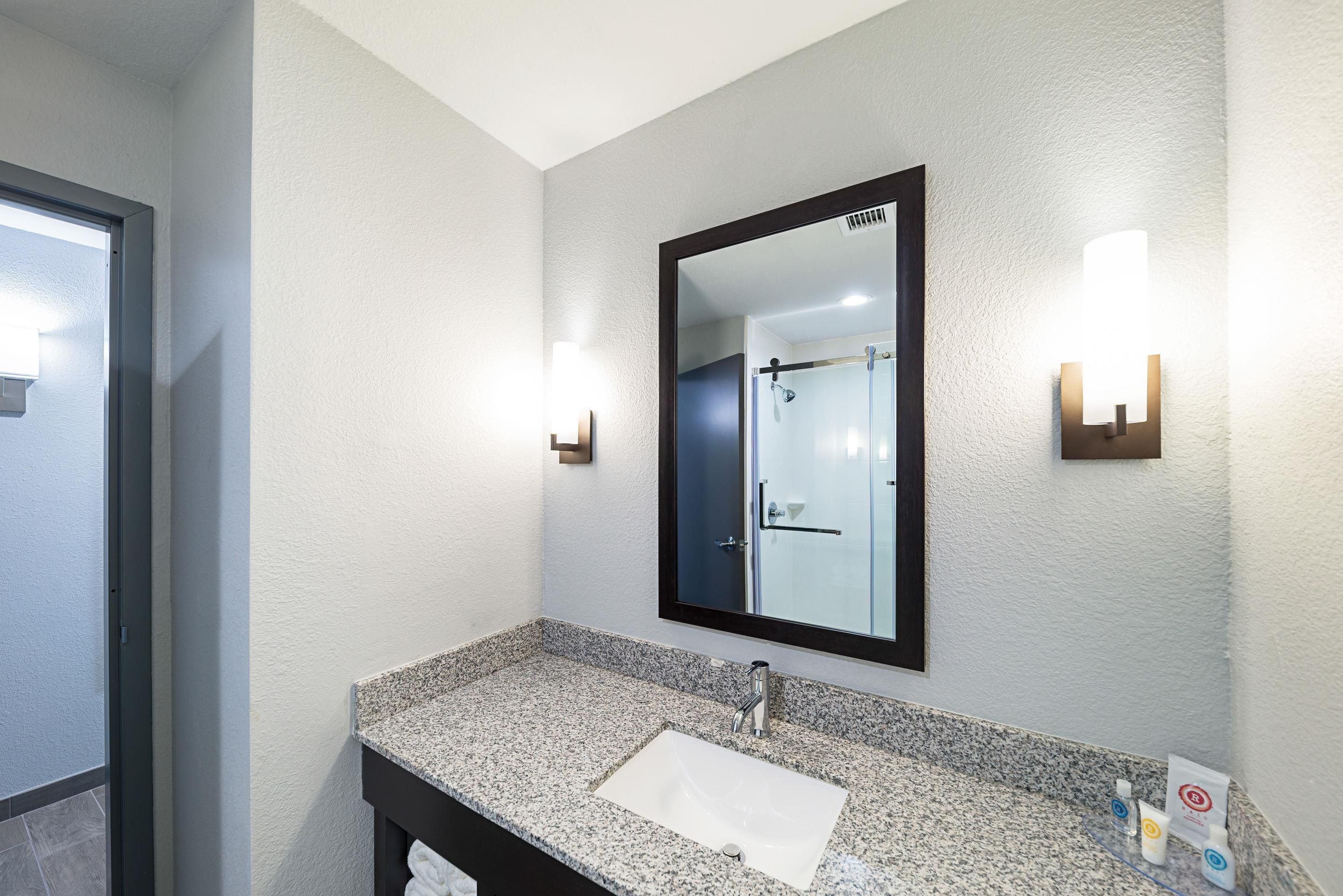 A bathroom with a granite countertop, a white sink, a large mirror, and two wall-mounted lights.