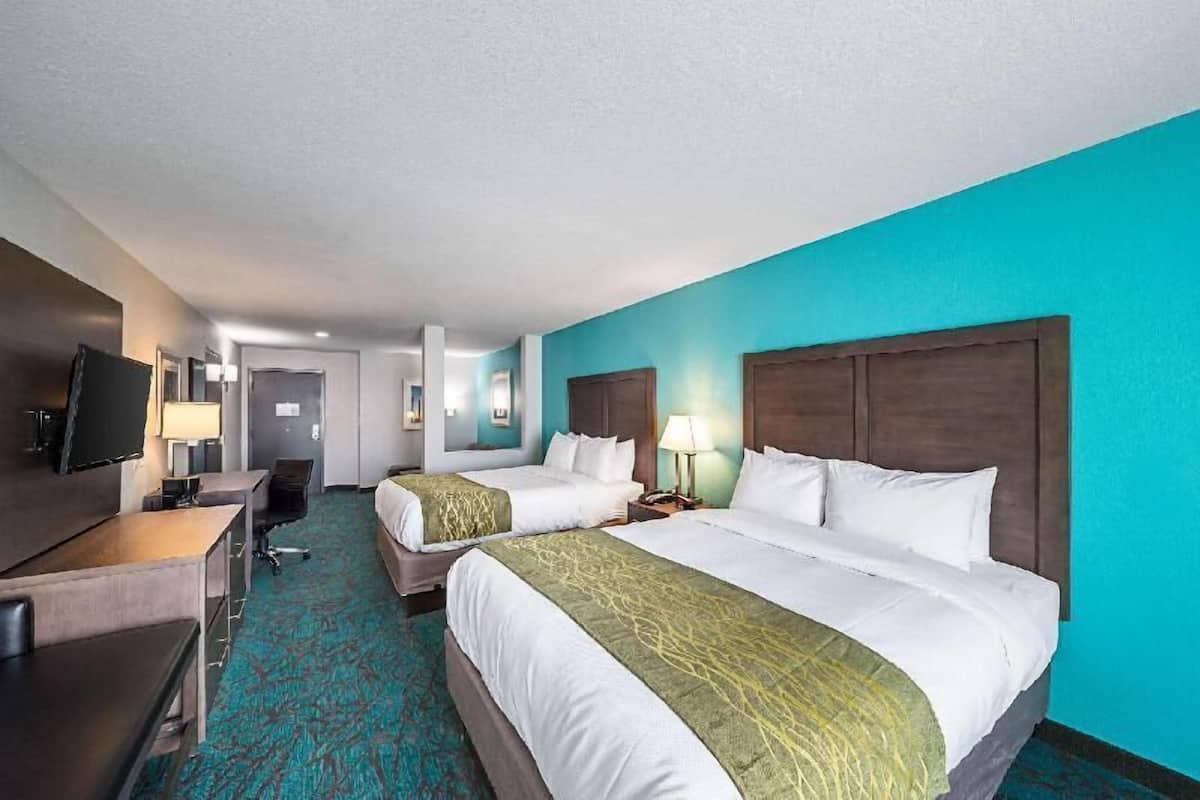 Ein Hotelzimmer mit zwei Betten, einem Schreibtisch, einem Fernseher und einem Badezimmer im Hintergrund.
