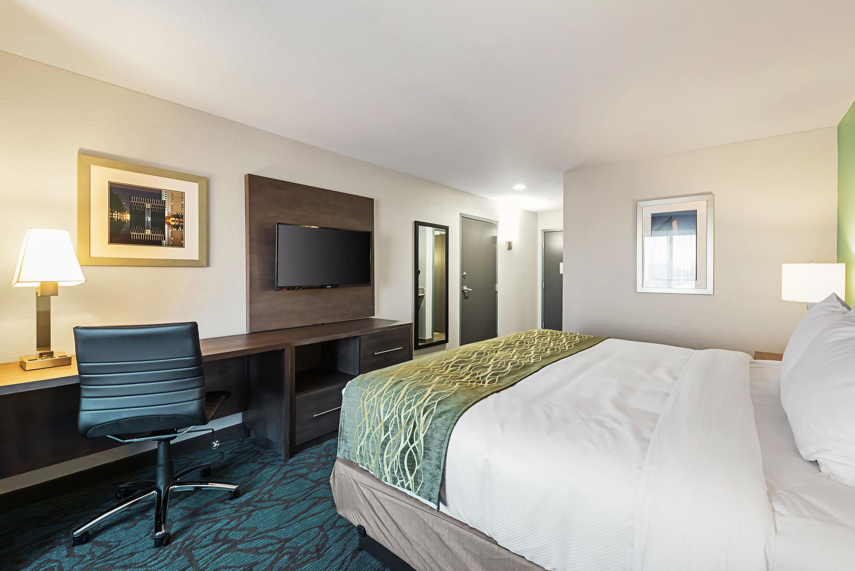 A hotel room with a bed, a desk with a chair, a television, and a door.