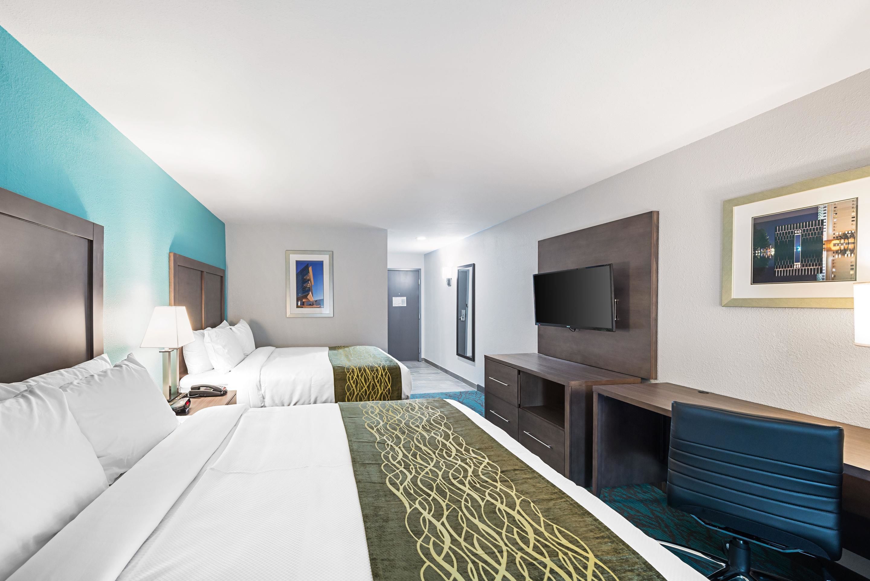 Une chambre d’hôtel avec deux lits, un bureau, une télévision et une salle de bain que l’on aperçoit à l’arrière-plan.
