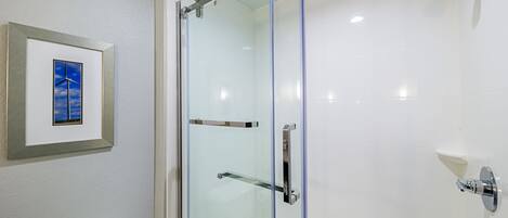 A modern bathroom with a glass shower enclosure, a framed picture on the wall, and a white toilet.