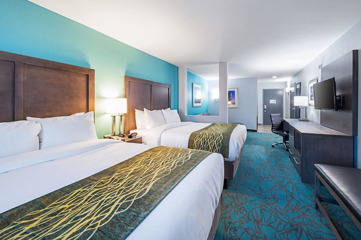 Ein Hotelzimmer mit zwei Betten, einem Schreibtisch, einem Fernseher und einem Badezimmer im Hintergrund.