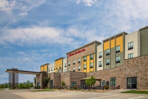 Un hotel moderno con fachada de piedra, varios pisos y un llamativo letrero de 'Hilton Garden Inn'.