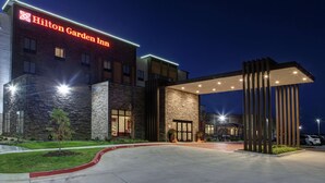 Un moderno Hilton Garden Inn con fachada de piedra, entrada amplia e iluminación exterior destacada.