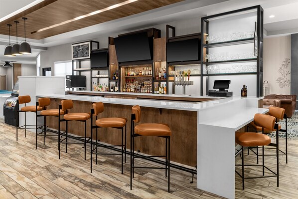 Eine moderne Bar mit einer langen Theke, mehreren Barhocker und einer Auswahl an Flaschen und Gläsern.