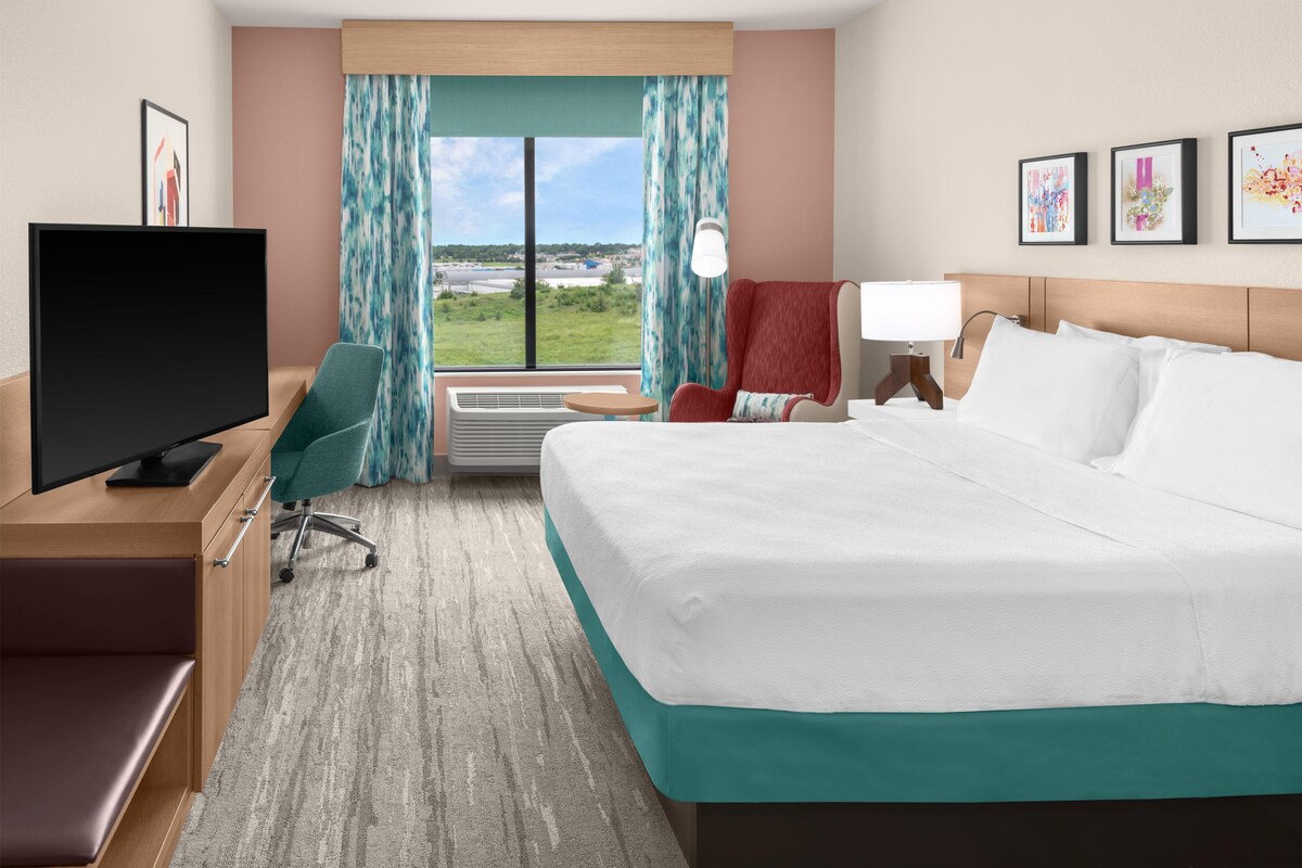 Habitación de hotel con cama, escritorio con televisor, silla, ventana con cortinas y vista al exterior.