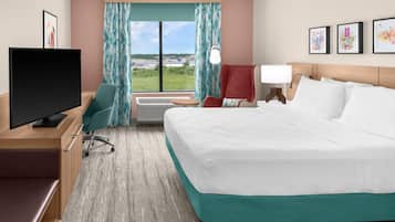 A hotel room with a bed, a desk with a television, a chair, a window with curtains, and a view of the outside.
