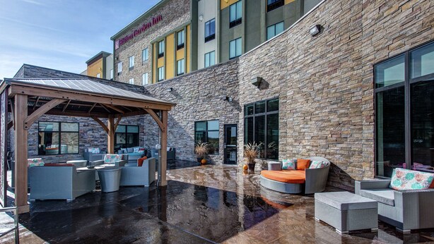 Un hotel con fachada de piedra, zona de estar al aire libre con mobiliario de mimbre y un porche cubierto.