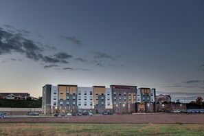 Hotel de vários andares com design moderno, com fachada em vidro e tijolo, e estacionamento em frente.