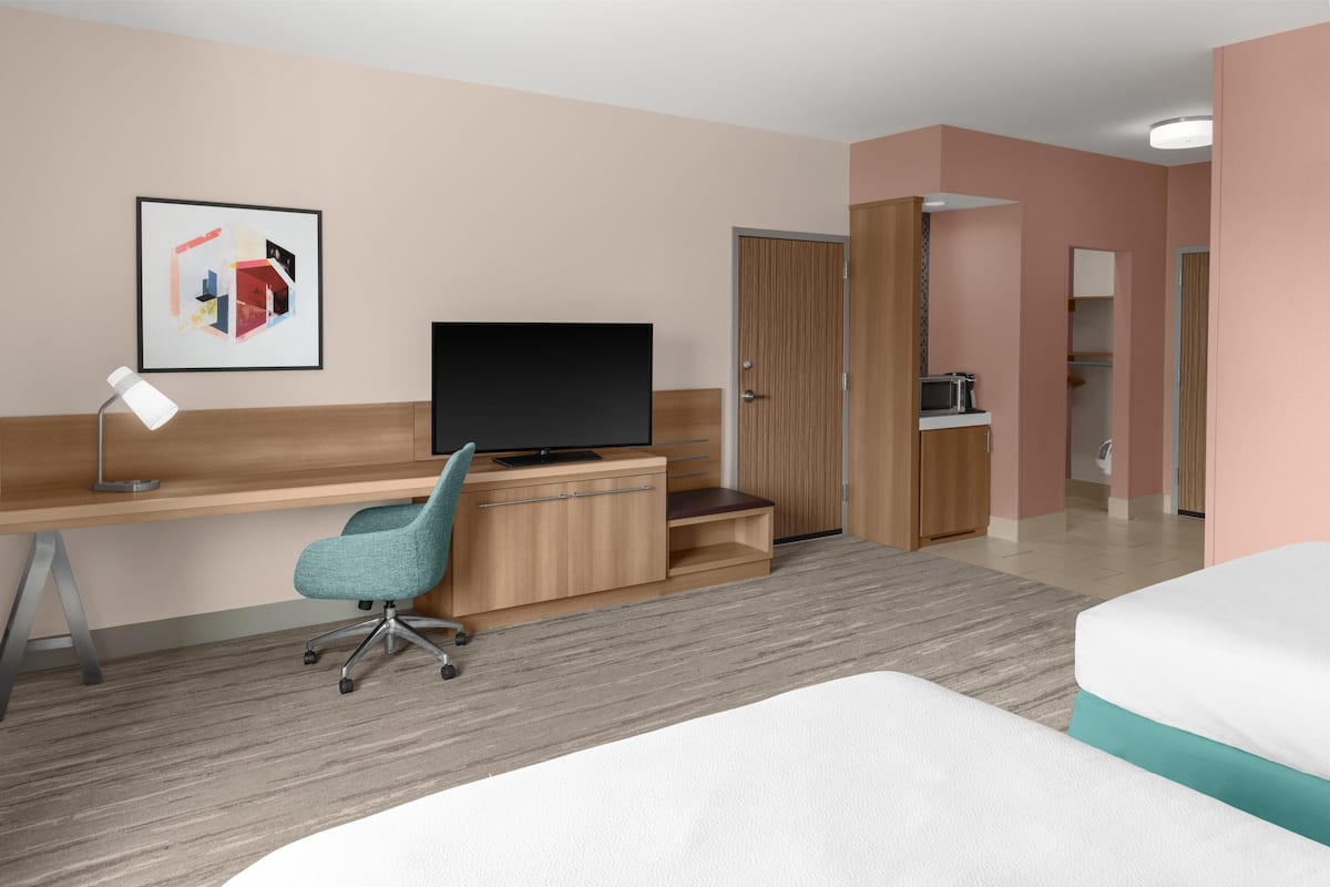 A hotel room with a bed, a desk with a computer, a TV, a chair, and a microwave.
